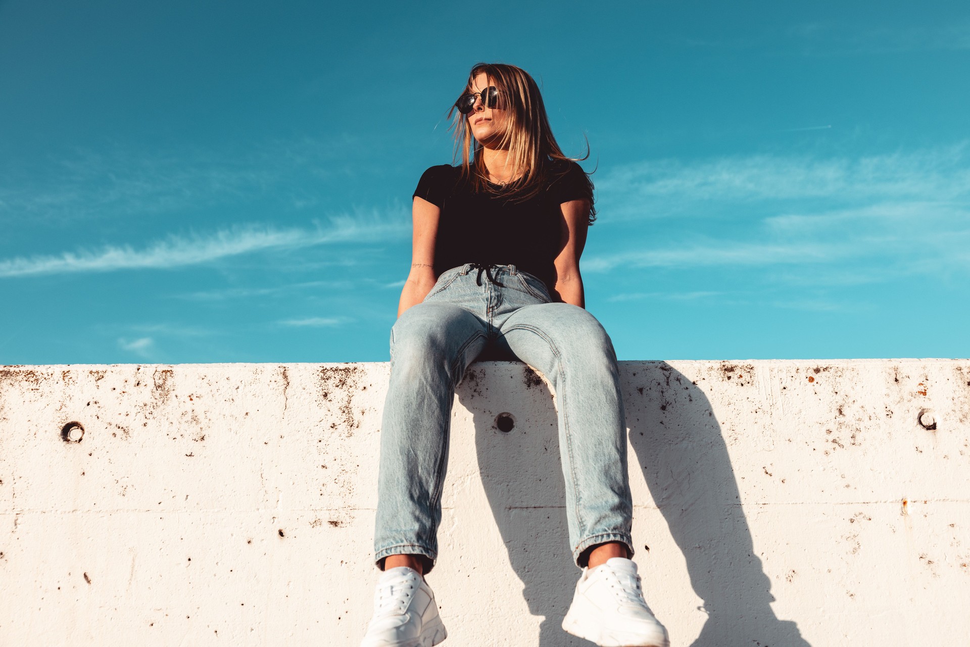 Cool Looking Young Woman Sitting on Concrete Wall With Sunglasses